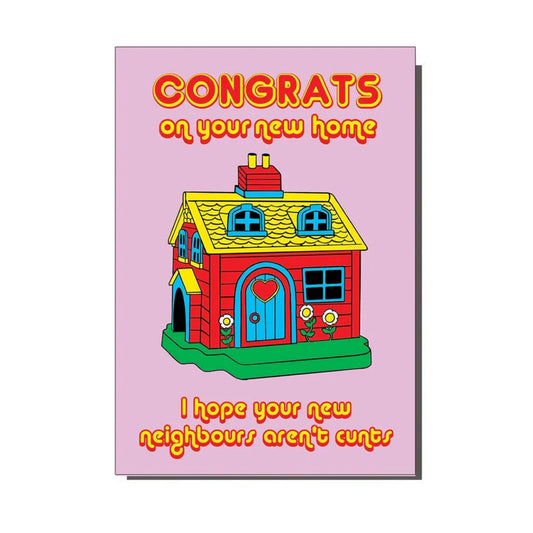 A pink greeting card with a drawing of a yellow, red and blue house on the front. The text on the card reads “Congrats on your new home, I hope your new neighbours aren’t cunts”