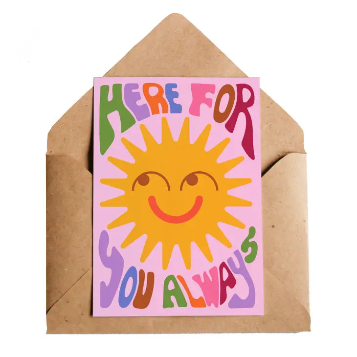 A pink card with a yellow smiling sun on the front. On the card there is writing that reads: '0Here for you always.' The letters are done in Green, purple, Orange, Blue, Pink, Brown and red 70's style bubble writing