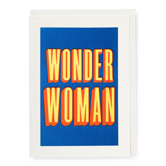 A letterpress printed greeting card with the text 'Wonder Woman' in bold orange and yellow letters on a blue background, with a white envelope.