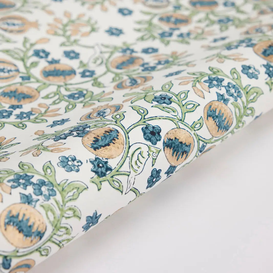A close-up view of a sheet of wrapping paper with a block printed floral pattern in blue and green colors on a white background.