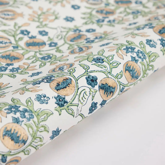 A close-up view of a sheet of wrapping paper with a block printed floral pattern in blue and green colors on a white background.
