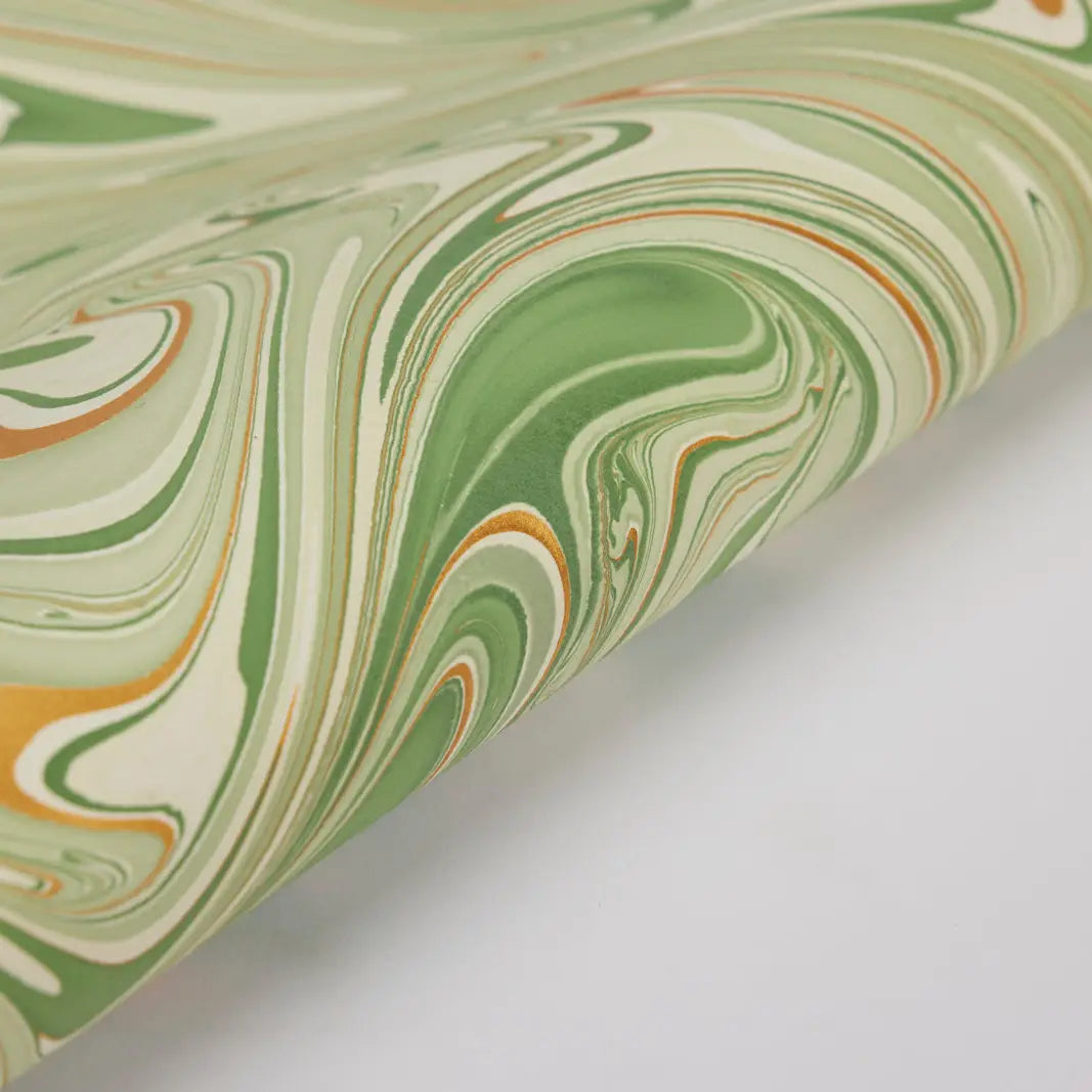 A close-up view of a hand marbled wrapping paper with green, white, and orange swirls.