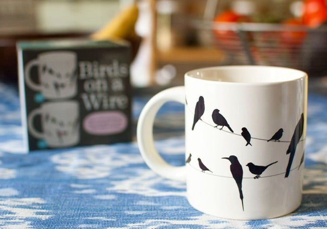 A cream mug with silhouettes of birds on a wire all over, when hot water is poured in they become colourful