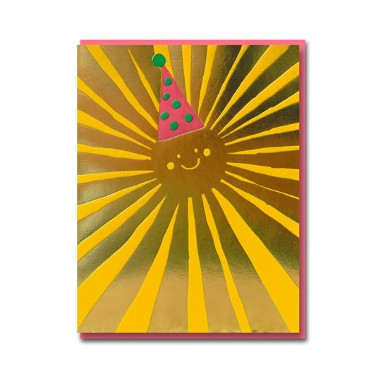 A birthday card with a yellow and metalic gold smiling sun in the centre that is wearing a pink and green birthday hat. 