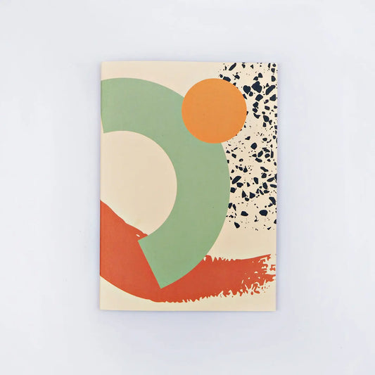 A rectangular notebook with a large green circle, a smaller orange circle, and a black and white speckled pattern on a light peach background.