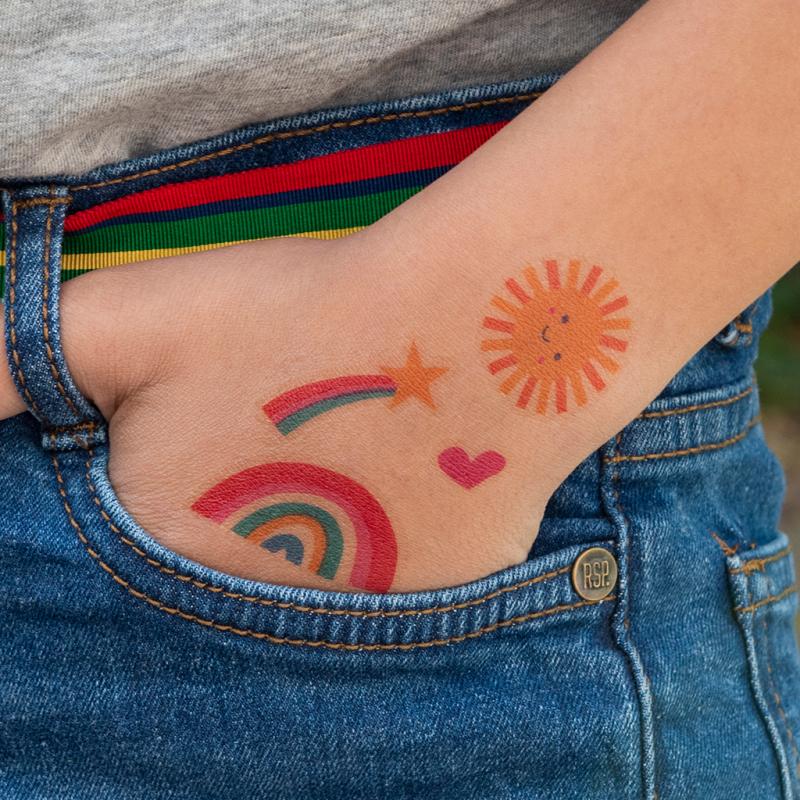 A hand tucked into a pocket with a sun, star, rainbow and heart temporary tattoo on.