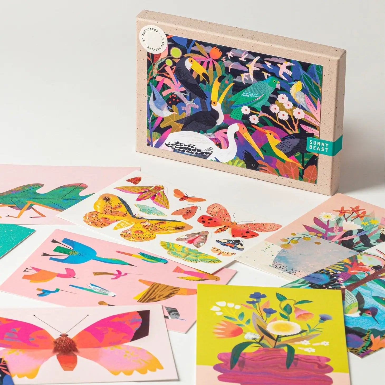 7  colourful postcards laid out in front the box, they are different postcards all with pictures of animals or flowers.