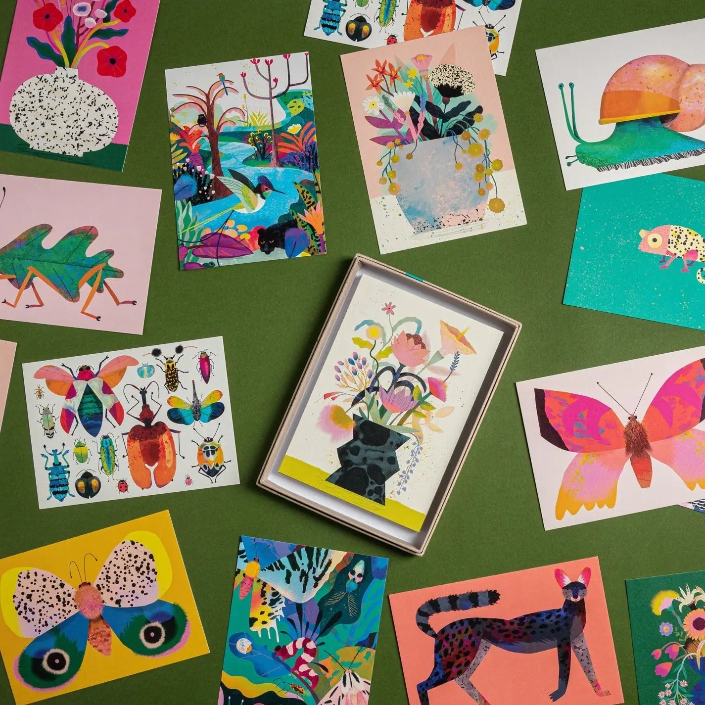 14 colourful postcards laid out on a table, they are different postcards containing pictures of animals or flowers. 