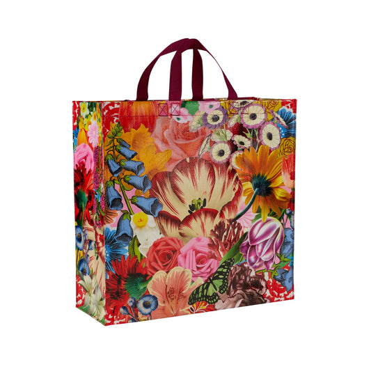 A floral tote bag with red handles. the flowers on the bag are Blue, red green yellow and pink.