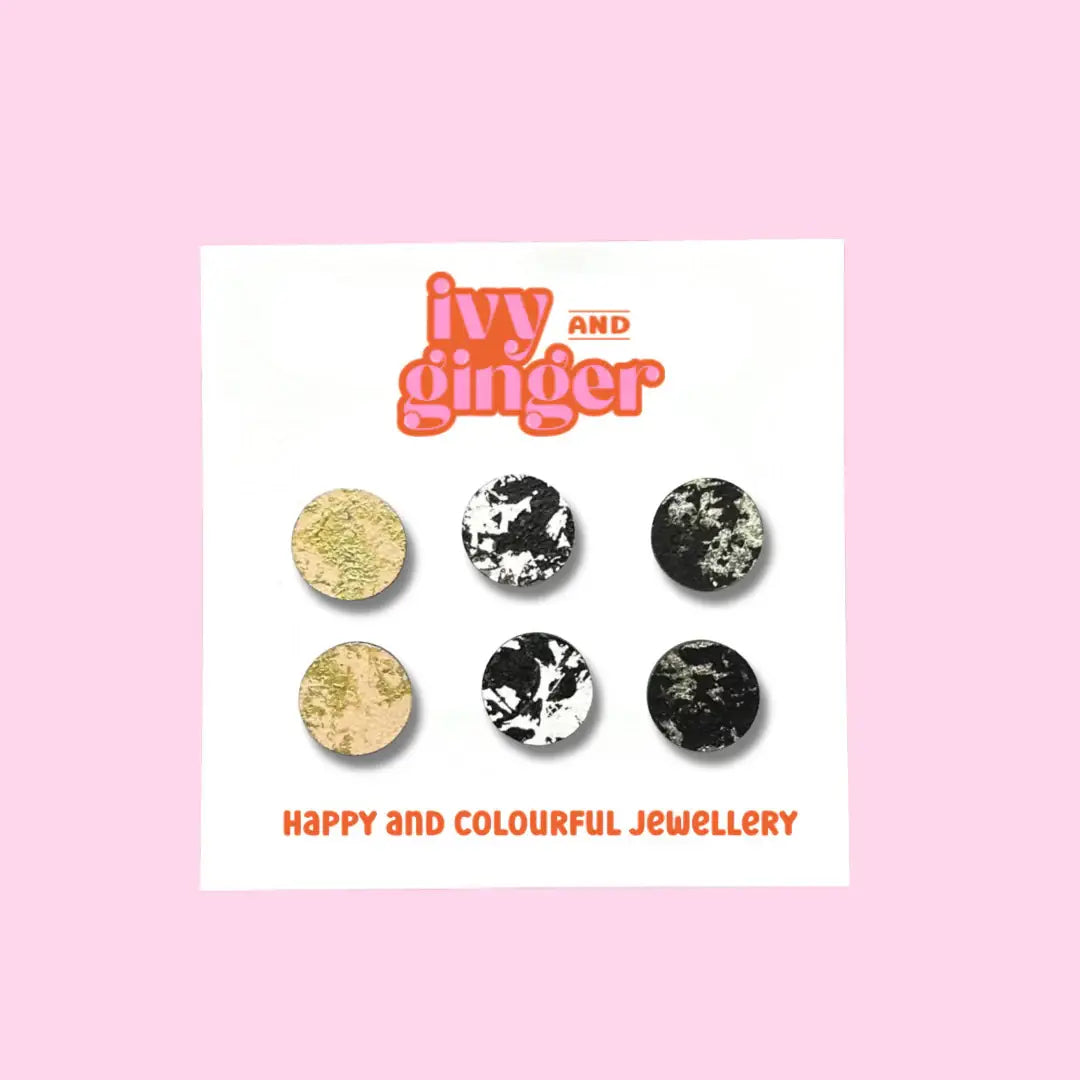 A set of round wooden earrings with a textured design, featuring colors such as black, white, and gold, displayed on a card with the brand name Ivy and Ginger.