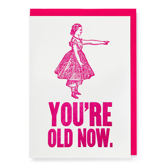 Greeting card with pink text 'YOU'RE OLD NOW.' and a stylized illustration of a girl on a white background.