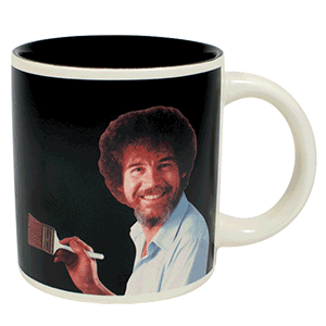 A mug with Picture of Bob Ross on. In the background it is black but shows it changes to one of his scenic paintings when filled with a hot liquid 