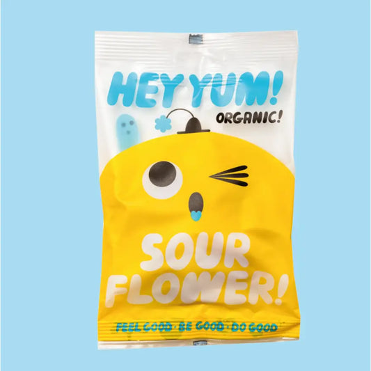 A white packet with a yellow winking character on the front. Behind him there is a small blue worm poking out and the text on the packet reads: The text on the pack reads: Hey, Yum! Sour flower! Organic . Feel good, Be good, Do good 