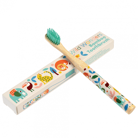 A wooden toothbrush with wild animal images on the handle is leaning up against a white cardboard box that reads: Faries in the garden bamboo toothbrush.