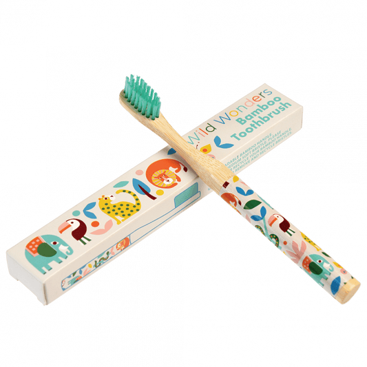 A wooden toothbrush with wild animal images on the handle is leaning up against a white cardboard box that reads: Faries in the garden bamboo toothbrush. 