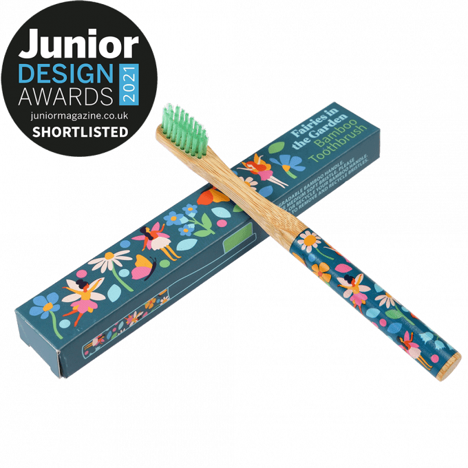 A wooden toothbrush with fairy images on the handle is leaning up against a blue cardboard box that reads: Faries in the garden bamboo thoothbrush. Junior Design awards 2021 shortlisted