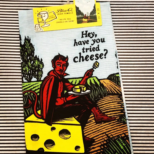 A Blue Q tea towel with the devil sat on a block of cheese in a field. 'Hey, have you tried cheese?'