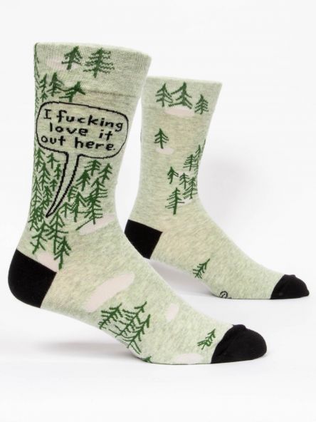 This image shows a pair of green men's socks with little trees on them. There is a speech bubble on them that reads i fucking love it out here