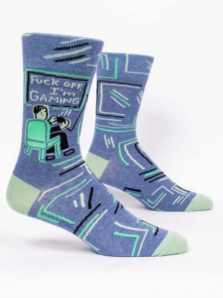 This image shows a pair of blue and green men's socks with an image of a boy sat in a chair gaming. The text on the socks says fuck off i'm gaming