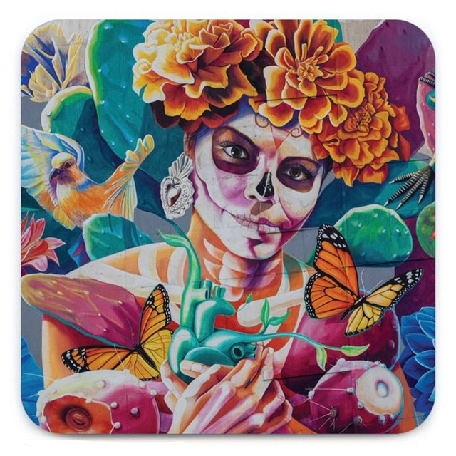 A coaster with a lady in the middle with skeleton face paint and a floral head band. Around her are colourful butterfly's, birds and other flowers.