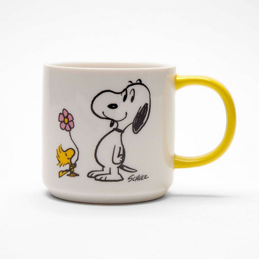 A white mug with a yellow handle. On the mug there is a graphic of Snoopy and Woodstock holding a flower.