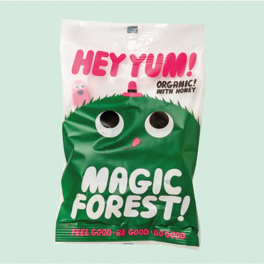 A white packet with a green fuzzy character on the front with a smiley worm  poking up behind him. The text on the pack reads: Hey, Yum! Magic forest! Organic with honey. Feel good, Be good, Do good 
