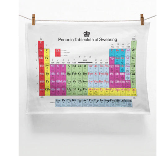 A tea towel hung on a washing line that has a periodic table printed on the front but instead of chemical elements it has swear words 