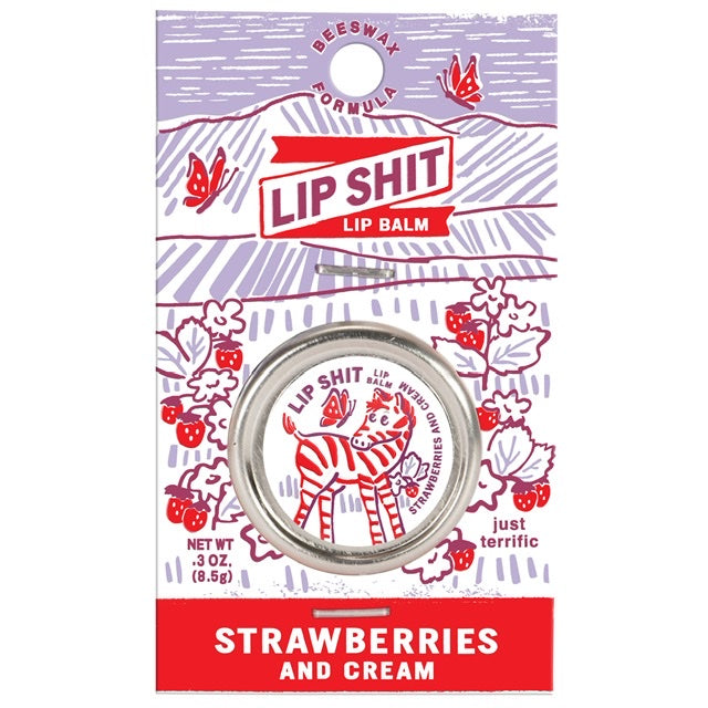 A Blue Q lip shit tin encased in purple cardboard packaging. The text reads: 'Lip shit lip balm Strawberries and cream'