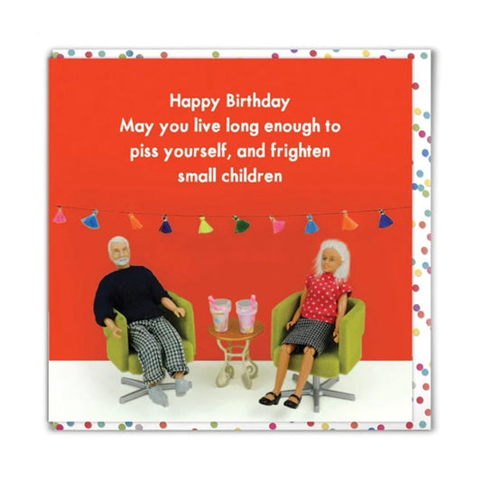This image shows a birthday card with the image of a cartoon elderly couple sat on chairs with some drinks in the middle of them. The text on the card reads 'Happy Birthday May you live long enough to piss yourself, and frighten small children.' The cards is red with some colourful bunting in the background and there is a spotty envelope 