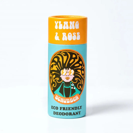 A Orange and blue cardboard tube containing eco friendly deodorant. In the middle is an image of a woman wearing sunglasses and her hair forms the word 'scrubber' The text on the tube reads: 'ylang & rose - scrubber - eco friendly deodorant'