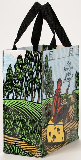 A Blue Q lunch bag with the devil sat on a block of cheese in a field. The text reads: 'Hey, have you tried cheese?'
