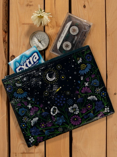 A Blue Q zipper pouch with purple, blue and green flowers around and white and yellow stars and a moon on the top