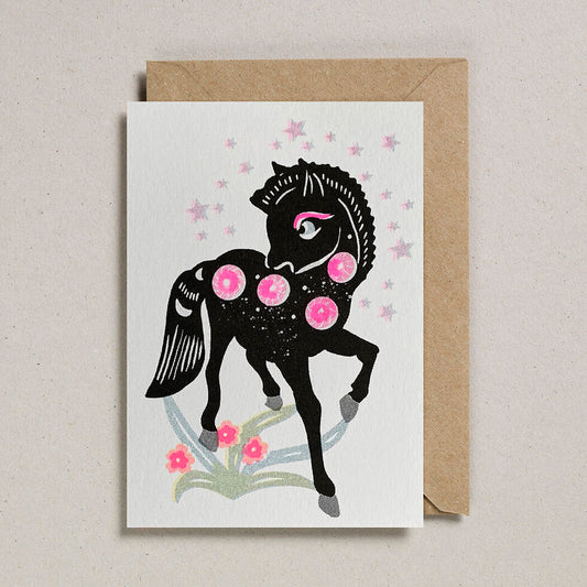 A white card with a print of a black horse on the front. The horse has pink circles on him and stars around him.