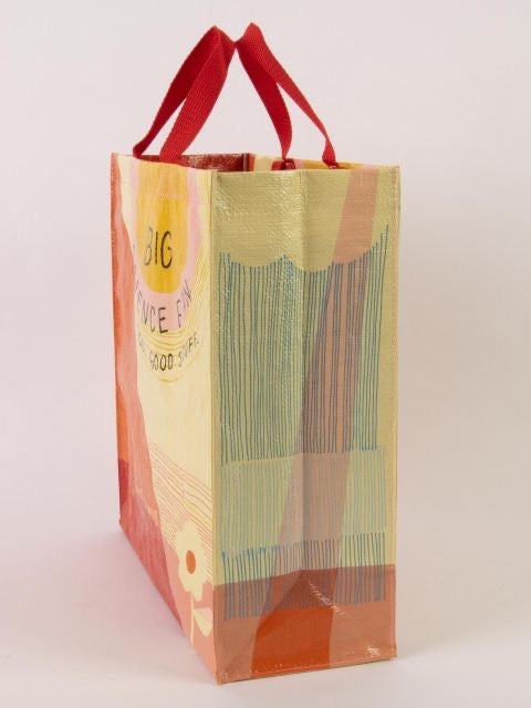 A yellow and orange Blue Q tote bag from the side. The bag has red handles and a flower in the bottom corner