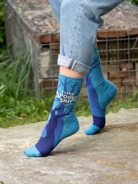 Someone wearing Blue Q ‘i like spooky shit’ socks whilst outside on the concrete with some grass in the background