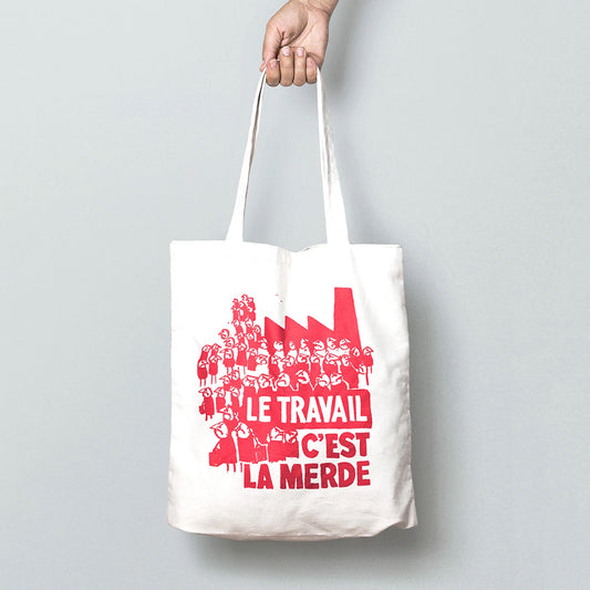 A white tote bag with a red drawings on of lots of grumpy people. The text on the bag reads: Le travail c'est la merde
