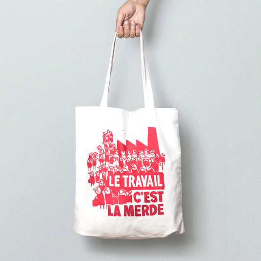 A white tote bag with a red drawings on of lots of grumpy people. The text on the bag reads: Le travail c'est la merde 