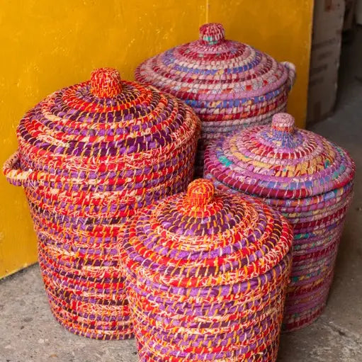 Set of colorful woven baskets with lids against a yellow wall.