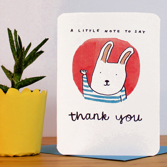Greeting card with cartoon rabbit and 'thank you' text on a wooden surface.