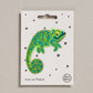 Embroidered chameleon patch on a white card with star patterns.
