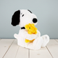 Plush toy of a dog holding a yellow duckling on a wooden floor with a gray background
