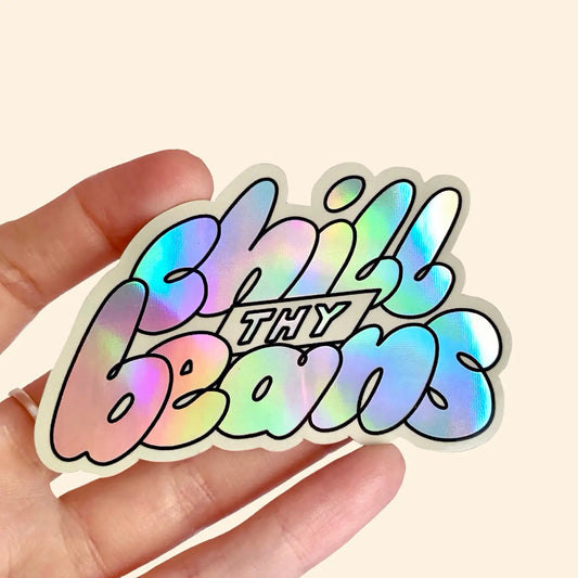 A holographic vinyl sticker with the text 'Chill Thy Beans' held in a person's hand.