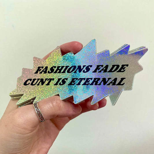 A holographic vinyl sticker with text 'FASHIONS FADE CUNT IS ETERNAL' held in a hand against a white background.