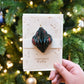 Hand holding a Christmas card with a decorative ornament against a festive background