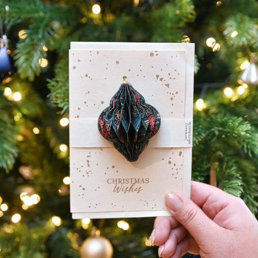 Hand holding a Christmas card with a decorative ornament against a festive background