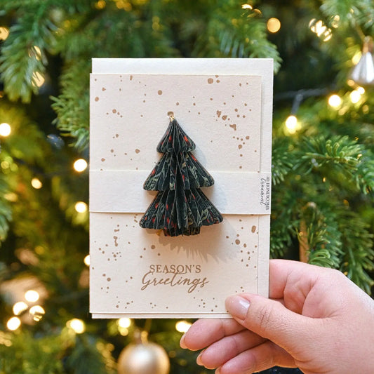 Card with a Christmas tree ornament held in front of a decorated Christmas tree.