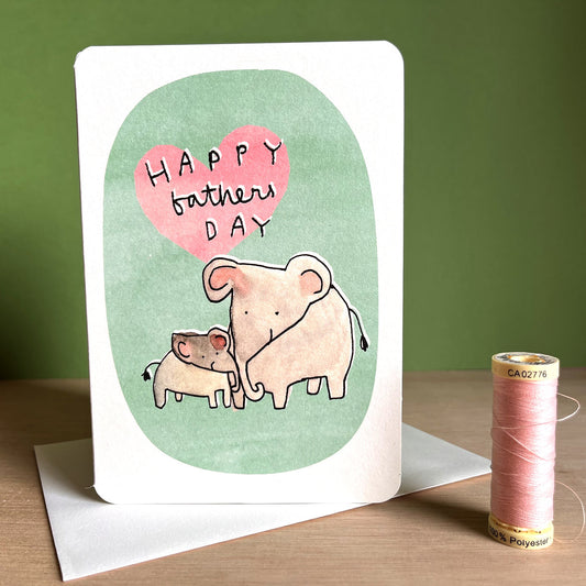 Father's Day card with cartoon elephants on a green background, next to an envelope and spool of thread.