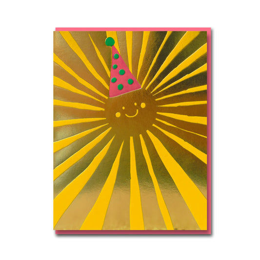 A birthday card with a yellow and metalic gold smiling sun in the centre that is wearing a pink and green birthday hat.
