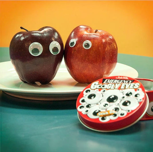 2 apples on a plate with a pair of googly eyes on them. Infront of them is a red tin that reads 'Emergency googly eyes'