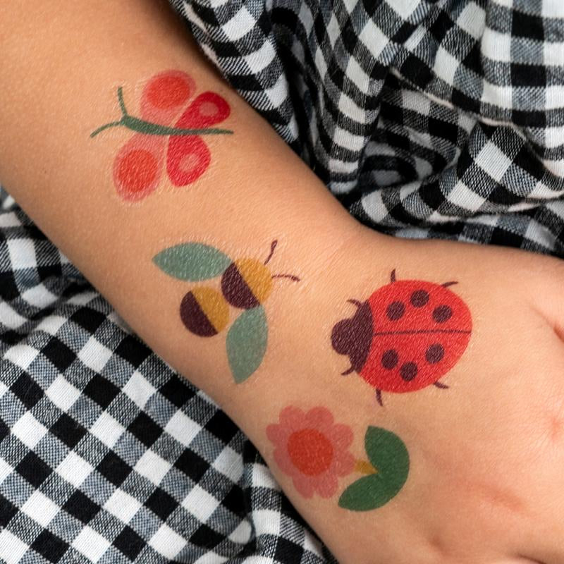 Someone’s hand with a ladybird, flower, bee and a butterfly temporary tattoo on.